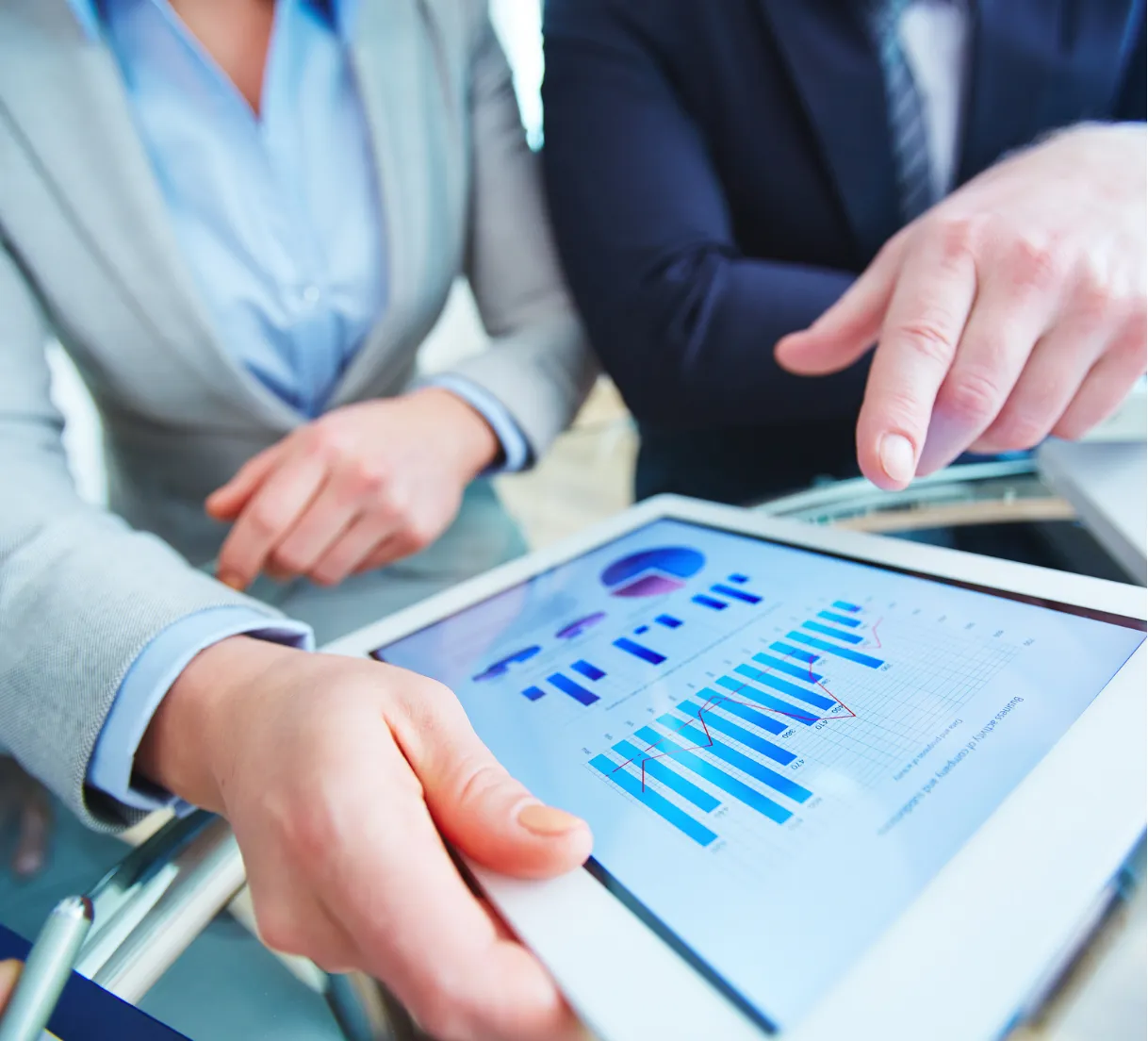 Two people reviewing financial bar charts on a tablet at a glass table, one person pointing at the screen.
