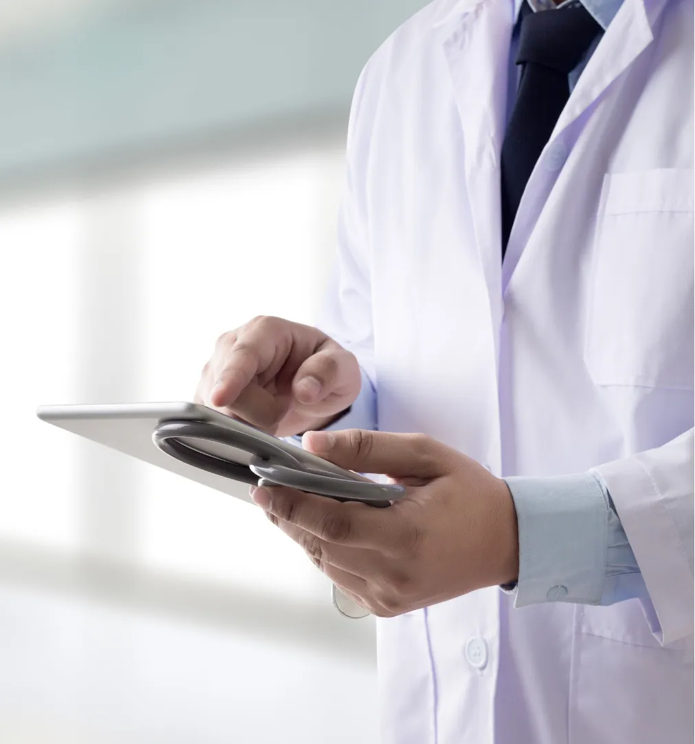 A doctor in a white coat using a tablet device in a bright, modern setting.