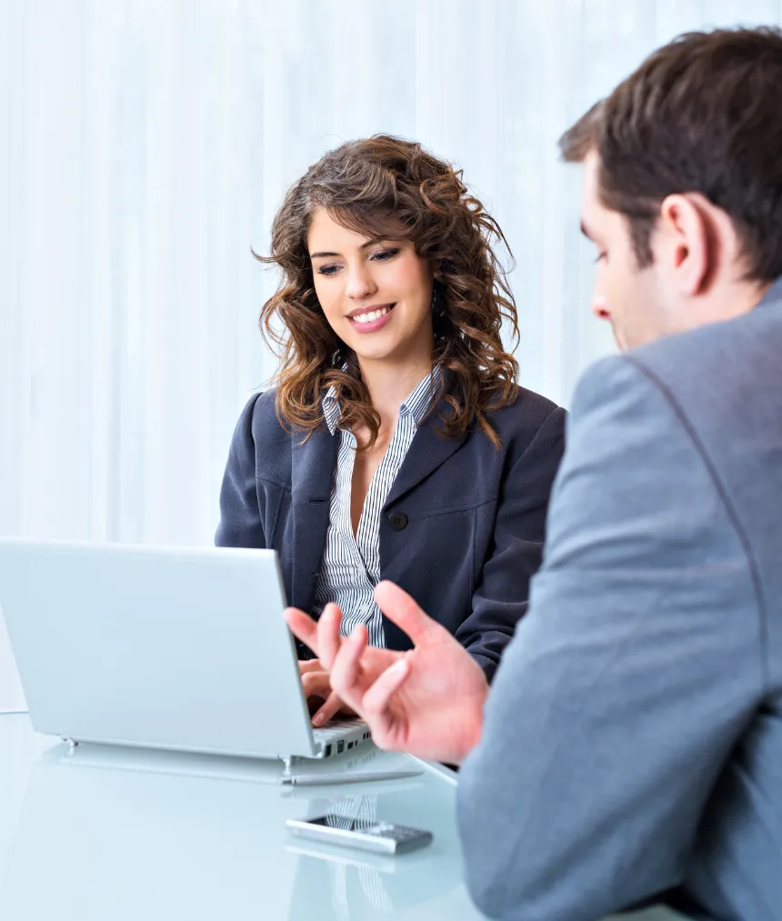 Two business professionals discussing something while working on a laptop at a desk.