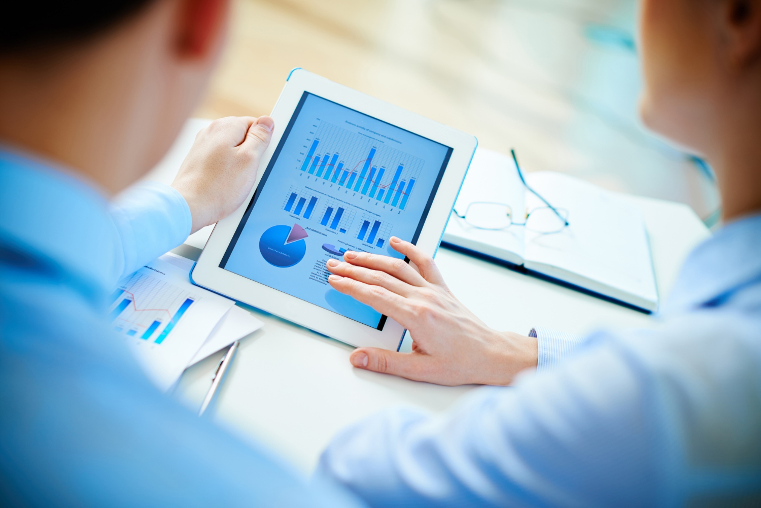 Two people reviewing colorful charts and graphs on a tablet screen during a business meeting.